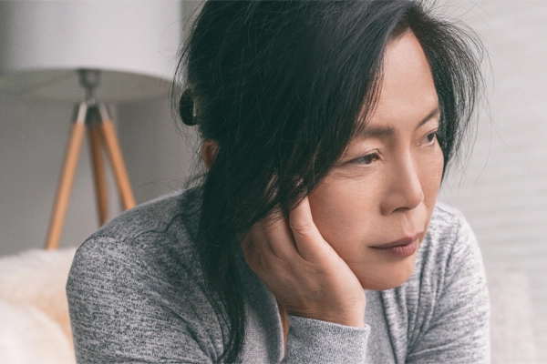 Adrenal-Fatigue-Doctor A middle-aged asian woman sitting on her couch, resting her head on her hand, suffering from adrenal fatigue. Get treatment for adrenal fatigue syndrome from Discovery Health Healing Center in Green Bay.