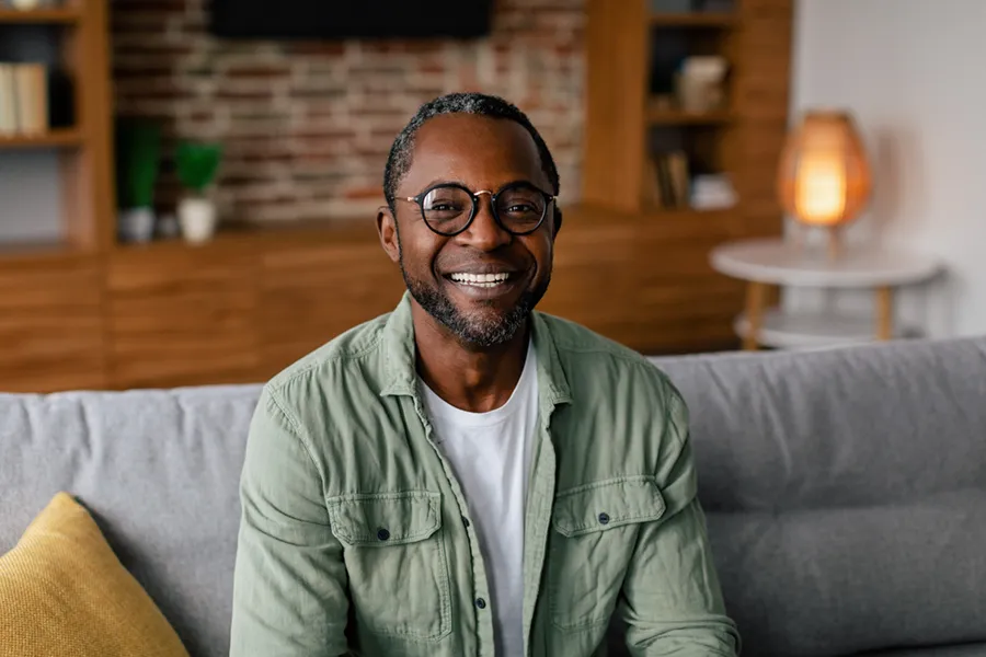 Andropause-Doctor A middle aged black man in a green button up shirt sits on his couch smiling, happy with his treatment for andropause and low testosterone from Discovery Health Healing Center in Green Bay.