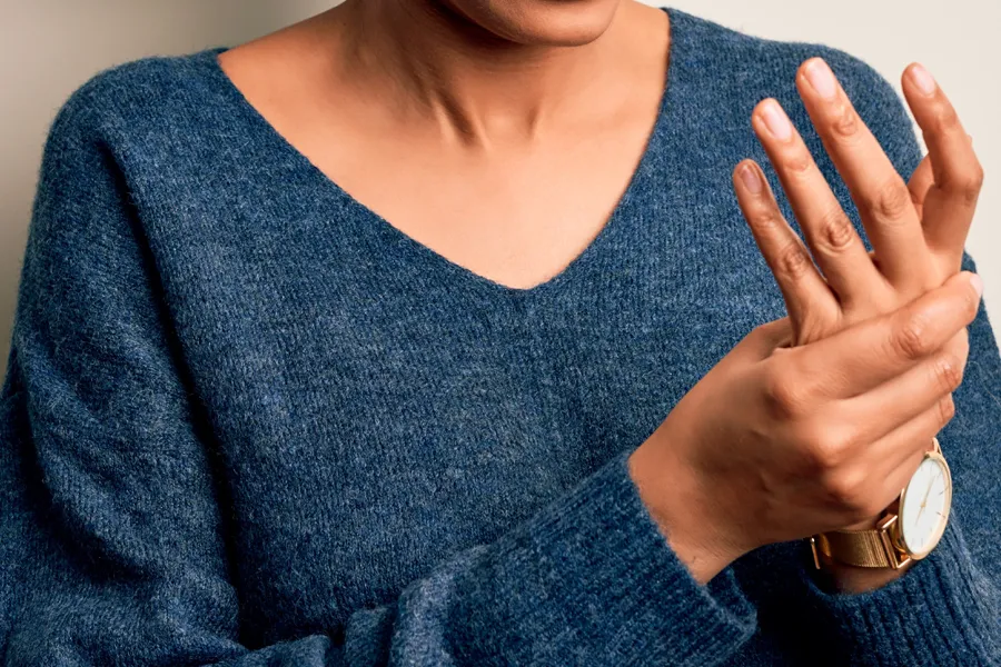 Arthritis-Doctor Close up of a woman in a blue sweater massaging one aching hand with the other. Get help for arthritis from Discovery Health Healing Center in Green Bay.