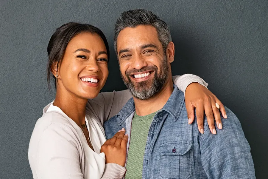 Bioidentical-Hormone-Therapy-Doctor A middle-aged couple with their arms around each other standing against a gray background and smiling, happy with the bioidentical hormone therapy they received from Discovery Health Healing Center in Green Bay.