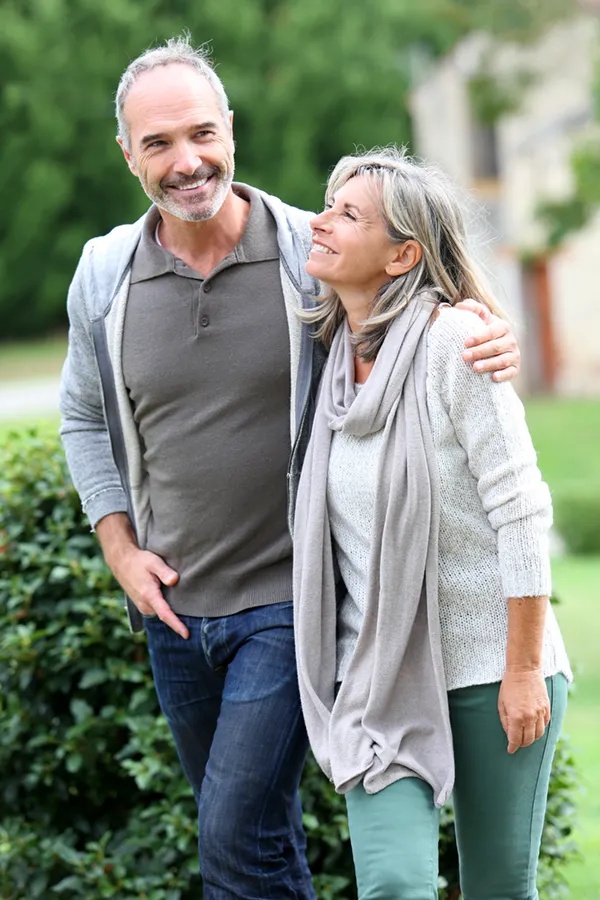 A mature couple in gray toned clothes and jeans walk happily outside, happy with their successful bioidentical hormone treatments from Discovery Health Healing Center in Green Bay.