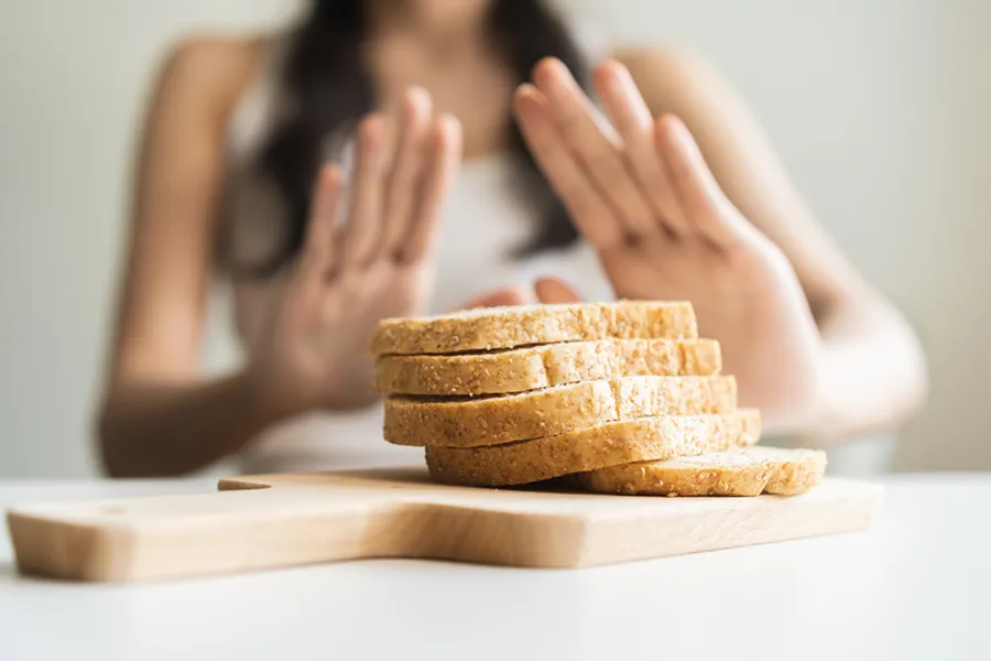 Celiac-Disease-Clinic Close up of a stack of bread slices on a cutting board with a woman's hands behind them, refusing to eat. Get treatment for Celiac Disease from Discovery Health Healing Center in Green Bay.