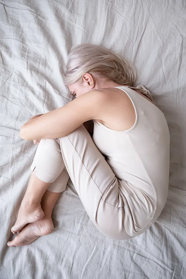 Chronic-Pain-Treatment A blonde woman curled up in the fetal position on the bed. Receive Insomnia treatment by Discovery Health Healing Center in Green Bay.