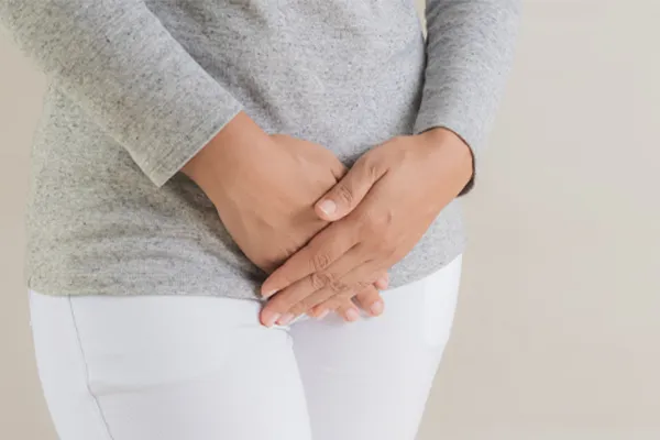 Fibroids-Clinic Close up of a woman in a gray shirt and white pants holding her hands below her abdomen in discomfort. Get treatment for fibroids from Discovery Health Healing Center in Green Bay.