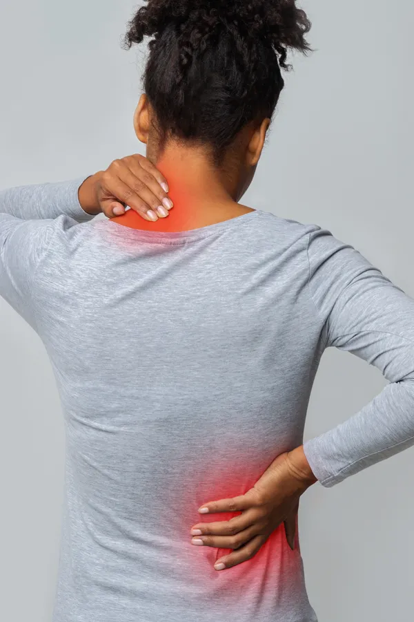 Fibromyalgia-Treatment An image from behind of a woman suffering from Fibromyalgia holding her hands on her neck and lower back. Get fibromyalgia treatment from Discovery Health Healing Center in Green Bay.