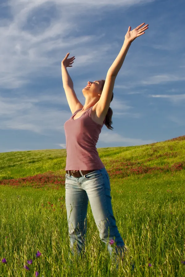 Graves-Disease-Treatment A woman in a tank top and jeans looks up with her arms outstretched to the sky in a field after successful treatment for Grave's Disease from Discovery Health Healing Center in Green Bay.