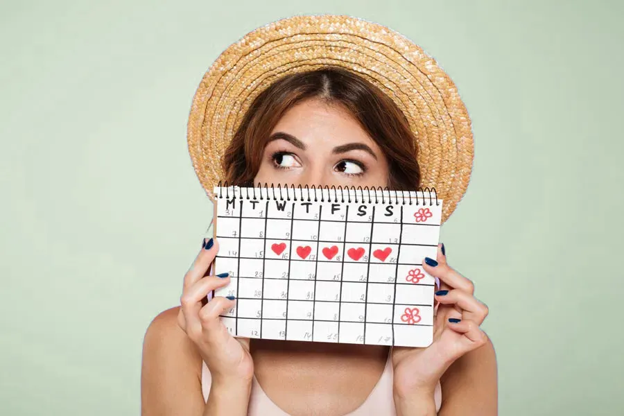 Menstrual-Dysfunction-Doctor A woman in a straw hat holds a calendar with several days marked off in front of her nose and mouth. Get treatment for menstrual dysfunction from Discovery Health Healing Center in Green Bay.