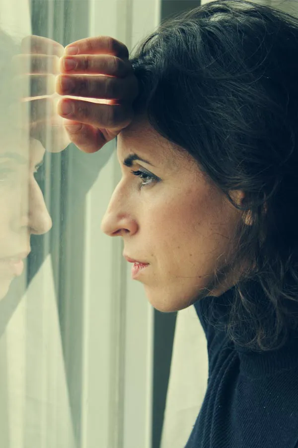 PCOS-Treatment A brunette woman in a thin dark turtleneck looks out the window with a serious expression, suffering from PCOS. Get treatment for Polycistic Ovarian Syndrome/PCOS from Discovery Health Healing Center in Green Bay.