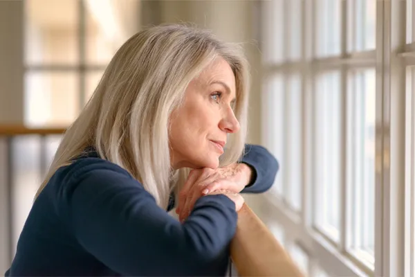 PMDD-Specialist A middle-aged woman with with a somber expression stares out the window. Get treatment for Premenstrual Dysphoric Disorder from Discovery Health Healing Center in Green Bay.