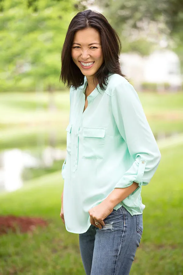 Perimenopause-Treatment A middle-aged brunette woman in a light green button-up shirt stands outside smiling, happy with her perimenopause treatment from Discovery Health Healing Center in Green Bay.