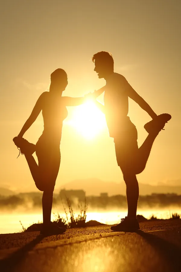 Regenerative-Medicine-treatment A couple stretching before exercise, silhouetted by the sunset. Get Regenerative Medicine treatment from Discovery Health Healing Center in Green Bay.