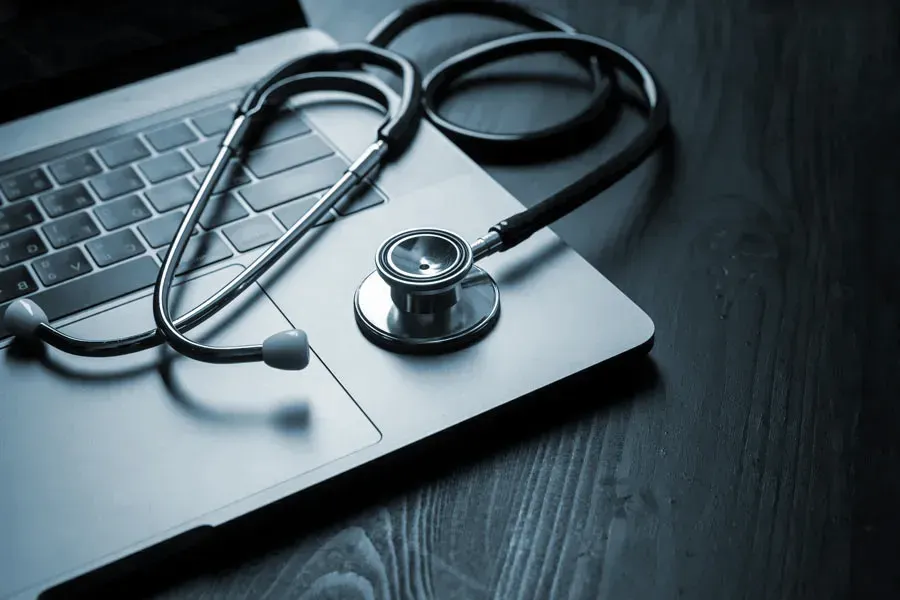 Telemedicine-Doctor An open laptop with a stethoscope lying on it on a wooden table, symbolizing telemedicine care from Discovery Health Healing Center in Green Bay.